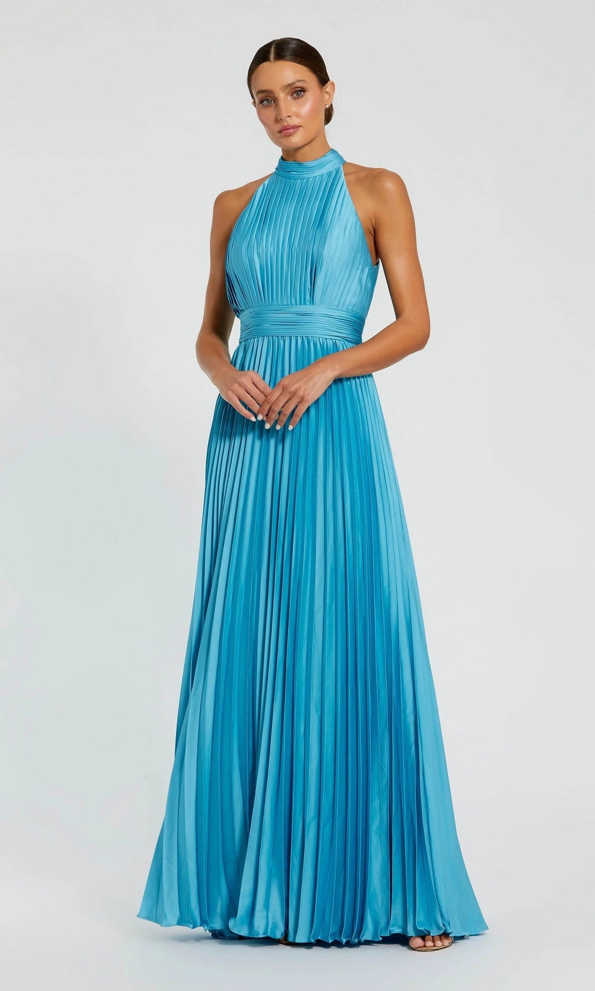 A woman stands against a plain light background wearing the Mac Duggal 26992 Long Pleated A-Line Formal Dress in pool blue, featuring a floor-length, sleeveless design with a high neckline.